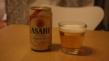 HD PC desktop wallpaper: Asahi beer can beside a poured glass on a wooden table with a warm indoor background — beer and food themed.