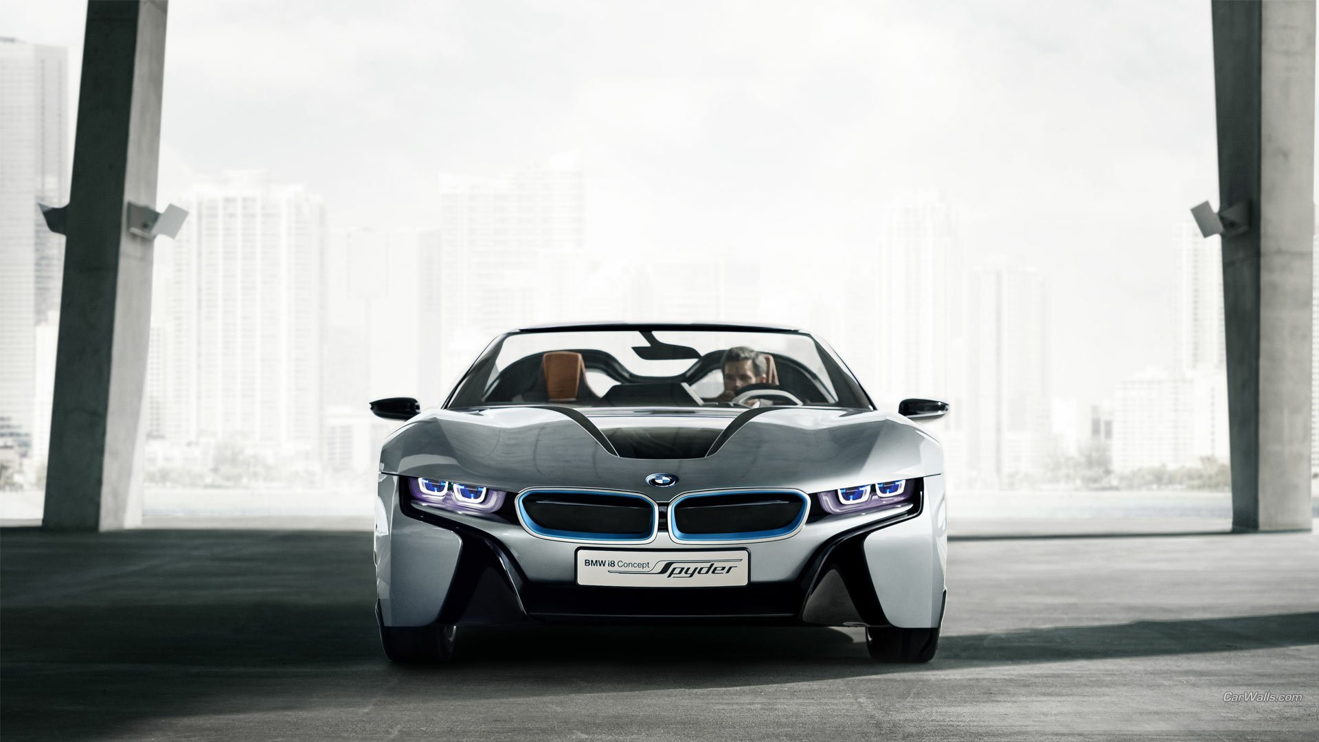 Front view of a silver BMW i8 Concept Spyder sports car rendered as an HD PC desktop wallpaper, parked against a soft urban skyline background.