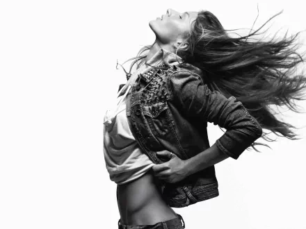 Black-and-white 2K Quad HD desktop wallpaper: dynamic celebrity portrait of a woman in a denim jacket, head thrown back, hair blowing, hands on hips, midriff exposed.