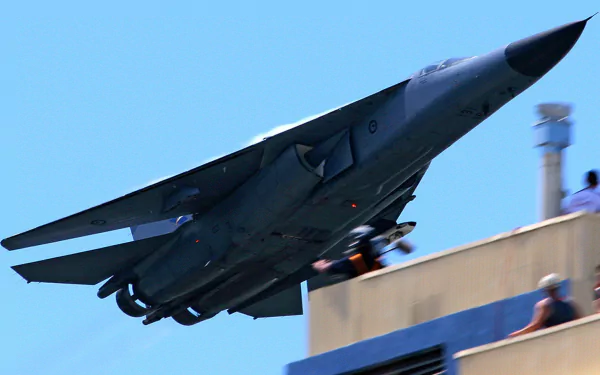 A General Dynamics F-111 Aardvark jet performs a steep ascent over a building, showcasing its military prowess in this HD desktop wallpaper.