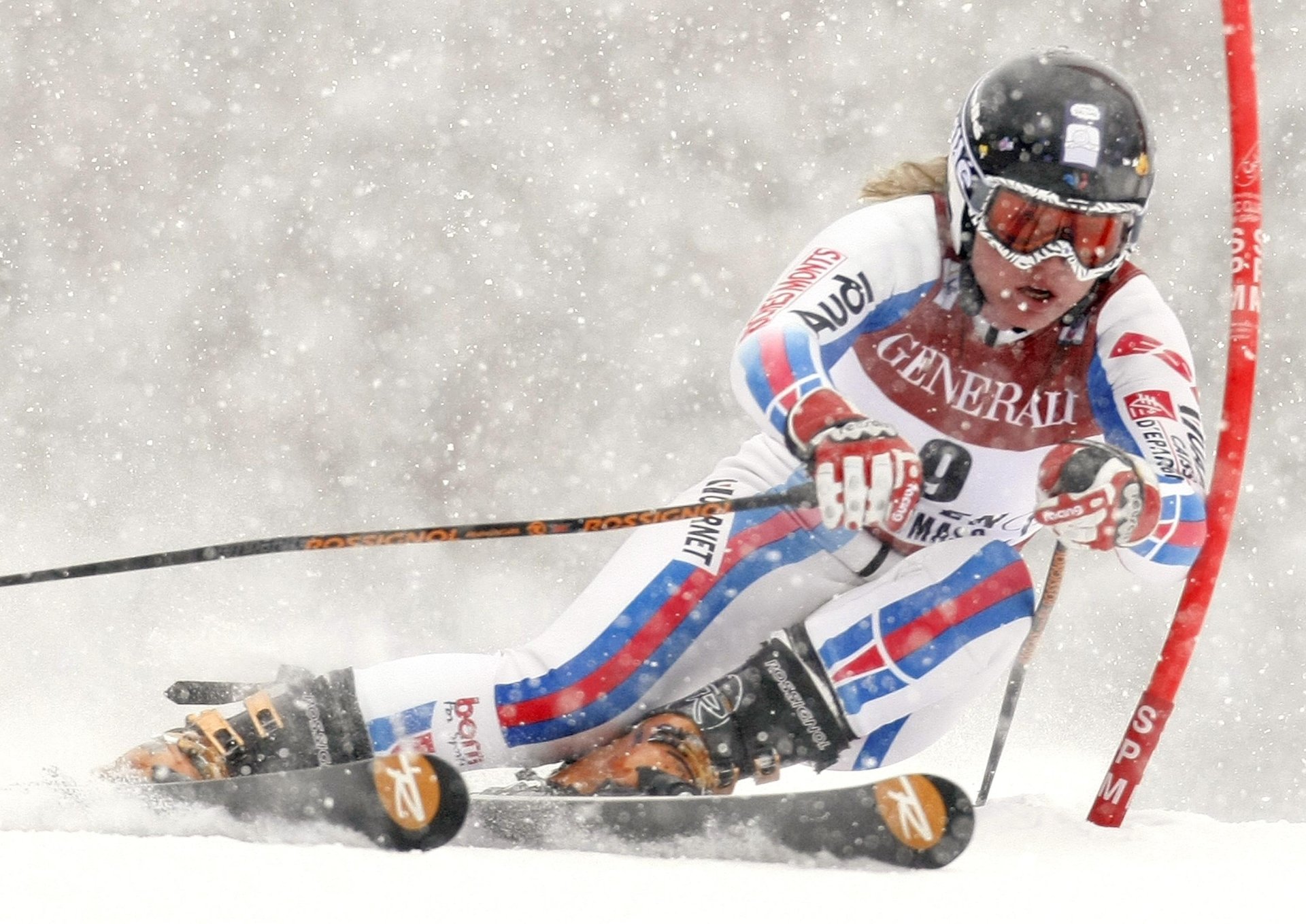 High-speed slalom skiing action: racer carving a turn through blowing snow around a gate, intense Sports scene rendered as a 2K Quad HD PC desktop wallpaper.
