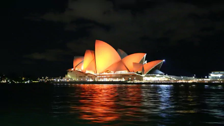 A stunning night view of the Sydney Opera House, illuminated against the dark sky, reflecting on the water, showcasing Australia's iconic man-made architectural beauty. 4K Ultra HD desktop wallpaper.