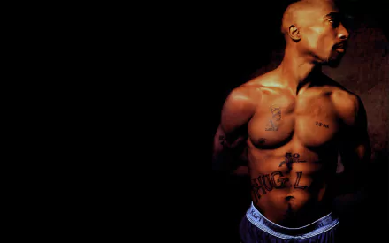 A striking HD desktop wallpaper featuring 2Pac, showcasing his tattoos and profile against a dark background, embodying his iconic presence in music history.