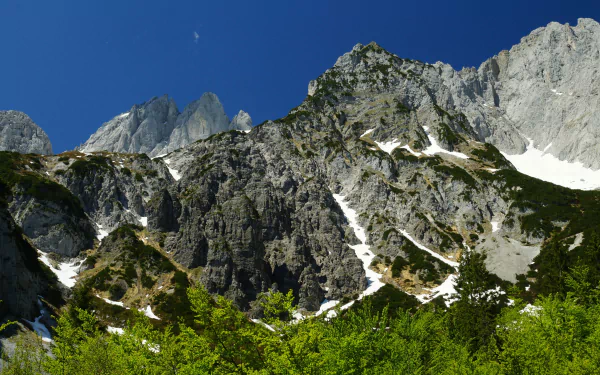 Stunning view of the Alps showcasing dramatic rocky peaks and lush greenery under a clear blue sky, captured in vibrant 4K Ultra HD for a breathtaking desktop wallpaper.