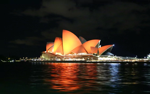 A stunning night view of the Sydney Opera House, illuminated against the dark sky, reflecting on the water, showcasing Australia's iconic man-made architectural beauty. 4K Ultra HD desktop wallpaper.