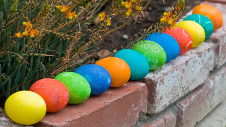 Colorful Easter eggs in vibrant hues line a brick pathway, surrounded by blooming plants, creating a cheerful holiday atmosphere. This HD wallpaper brings festive charm to any desktop.