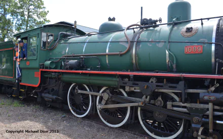 HD desktop wallpaper depicting a vintage green locomotive train with detailed wheels and steam engine components, set against a natural outdoor background.