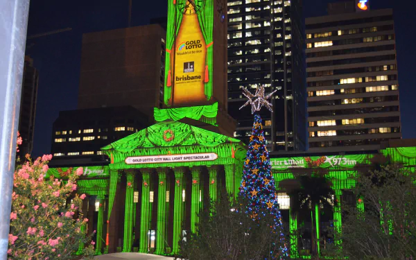 Brisbane City Hall illuminated in green light at night, with a decorated Christmas tree in front and surrounding city buildings, captured as a HD desktop wallpaper.