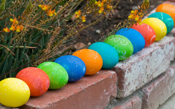 Colorful Easter eggs in vibrant hues line a brick pathway, surrounded by blooming plants, creating a cheerful holiday atmosphere. This HD wallpaper brings festive charm to any desktop.