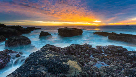 A stunning HDR image of a peaceful beach at sunset, showcasing vibrant colors reflecting off the ocean, with rocky formations and gentle waves creating a serene natural scene.
