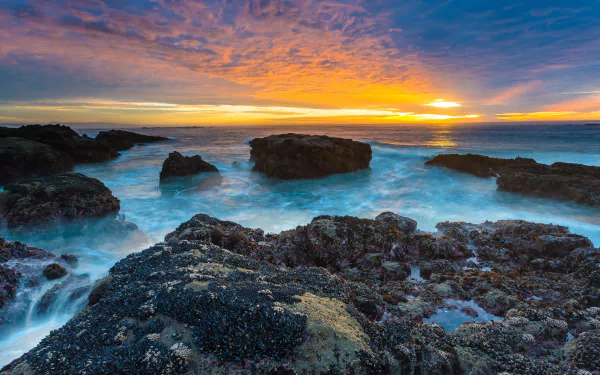 A stunning HDR image of a peaceful beach at sunset, showcasing vibrant colors reflecting off the ocean, with rocky formations and gentle waves creating a serene natural scene.