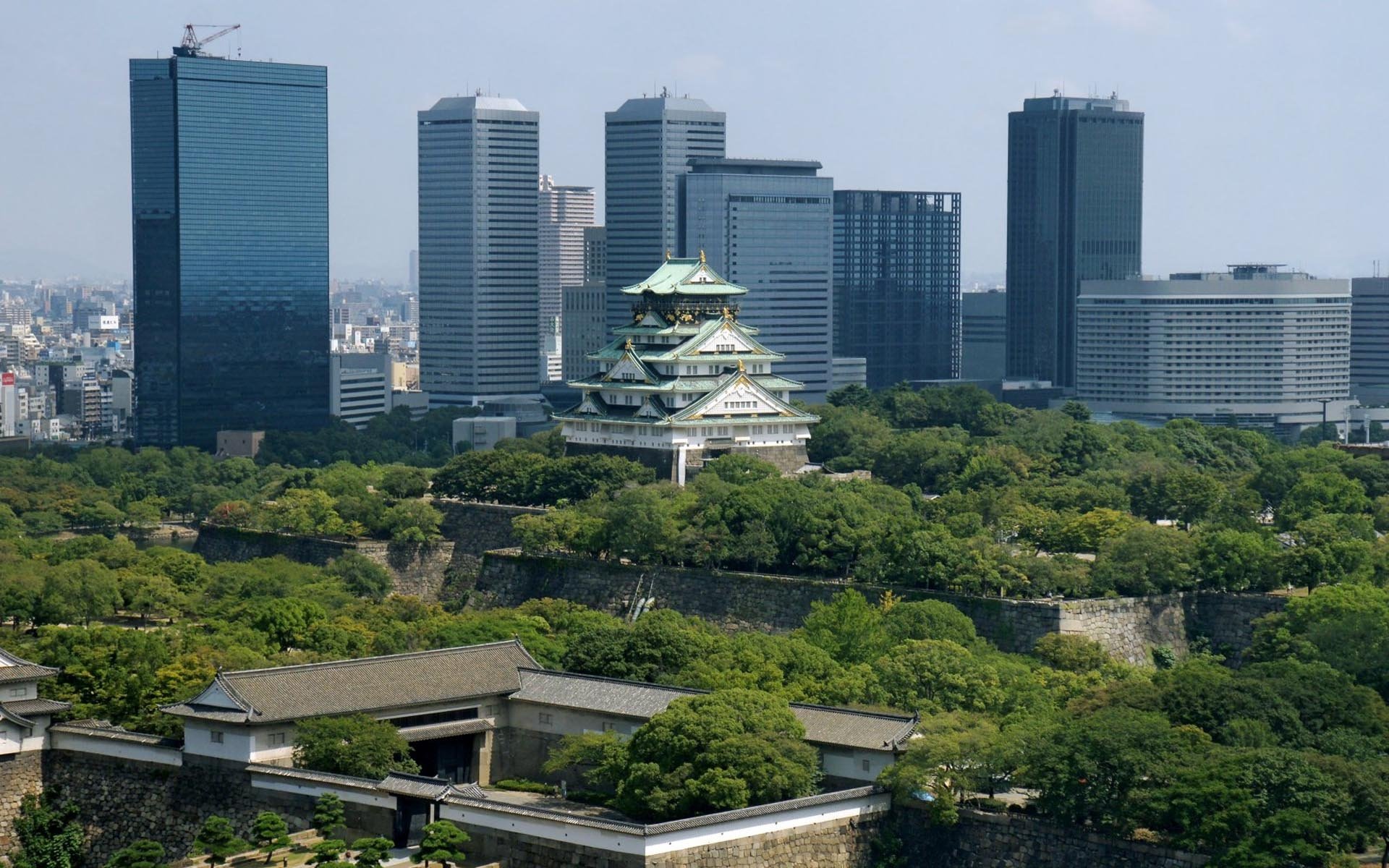 HD desktop wallpaper featuring Osaka's historic castle surrounded by lush greenery and modern skyscrapers in the background, highlighting a man-made urban landscape.