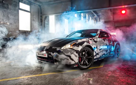 HD desktop wallpaper featuring a Nissan 370Z Nismo with a camo wrap, parked in a smoky, dimly lit industrial garage.