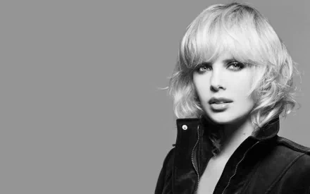 Black and white HD desktop wallpaper of celebrity Charlize Theron with short blonde hair, wearing a dark jacket against a plain gray background.