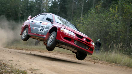A dynamic Mitsubishi Lancer Evolution leaps off a dirt road, surrounded by greenery, showcasing its performance in action. This HD wallpaper captures the thrill of rally driving.