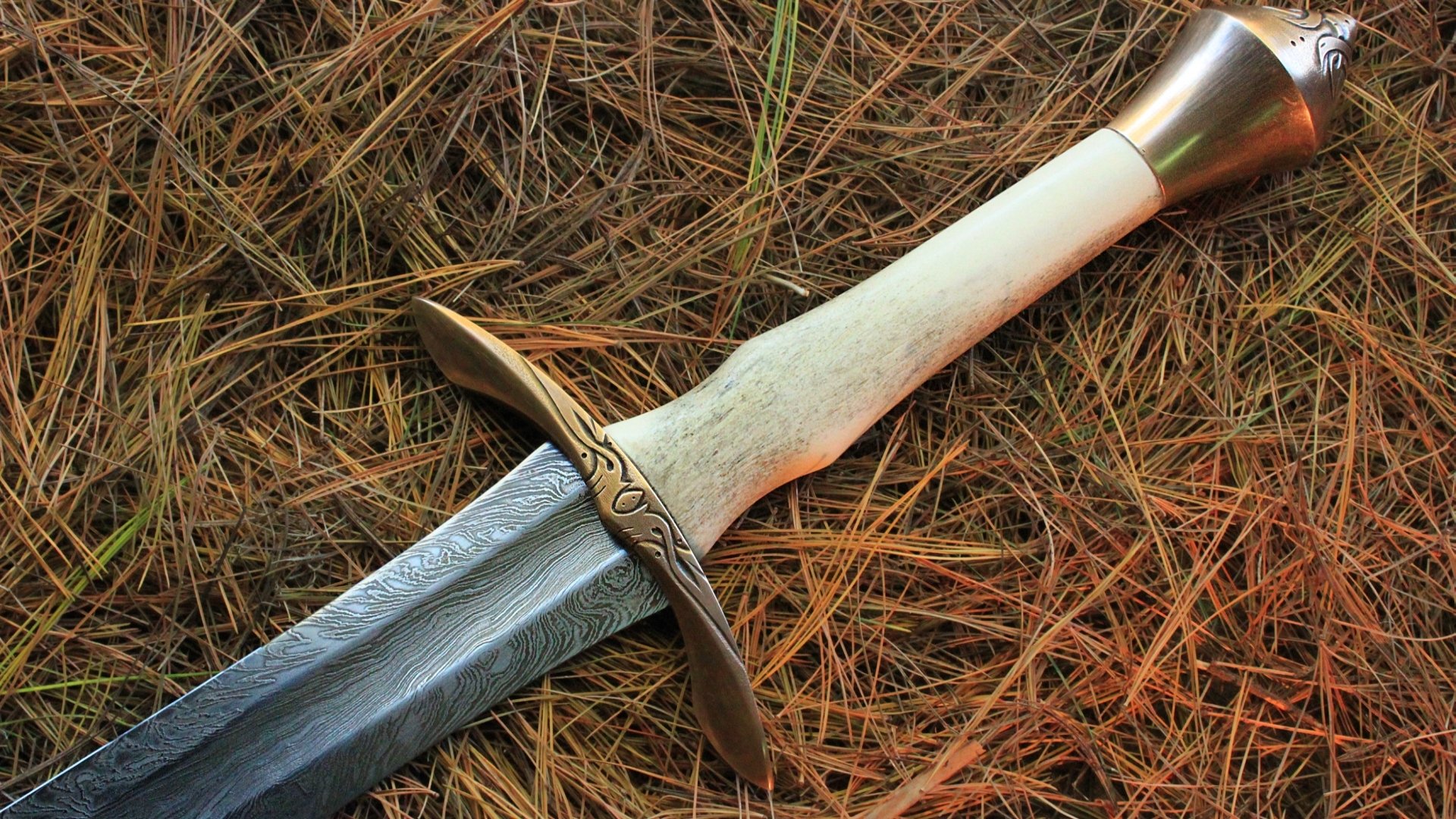 HD desktop wallpaper featuring a detailed man-made sword with a bone-colored handle resting on dry grass.