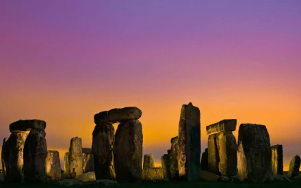 HD PC desktop wallpaper of Stonehenge, the iconic man-made stone circle, set against a vibrant sunset sky with purple and orange hues.