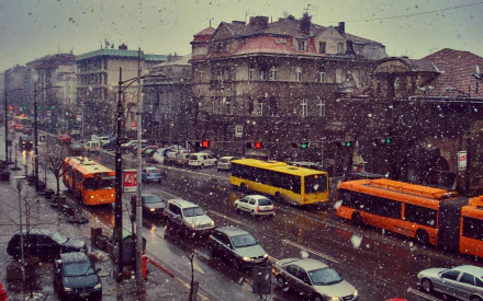 Winter scene in Belgrade with snow falling over busy streets filled with buses and cars, captured in sharp HD detail as a cityscape wallpaper.