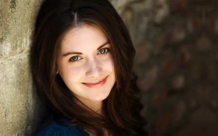A high-definition desktop wallpaper featuring celebrity Alison Brie, showcasing her beautiful smile and striking blue eyes against a textured wall background.