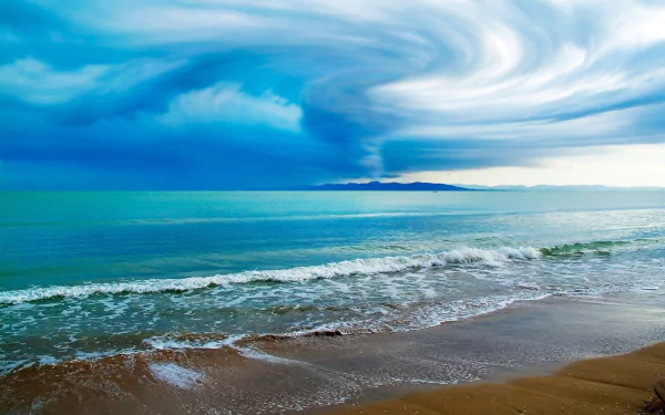 HD desktop wallpaper capturing a storm over the ocean with dramatic swirling clouds and waves crashing onto a sandy shore, showcasing powerful natural scenery.