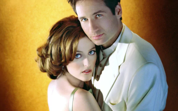 HD PC desktop wallpaper featuring actors David Duchovny and Gillian Anderson posing closely against a warm yellow background.