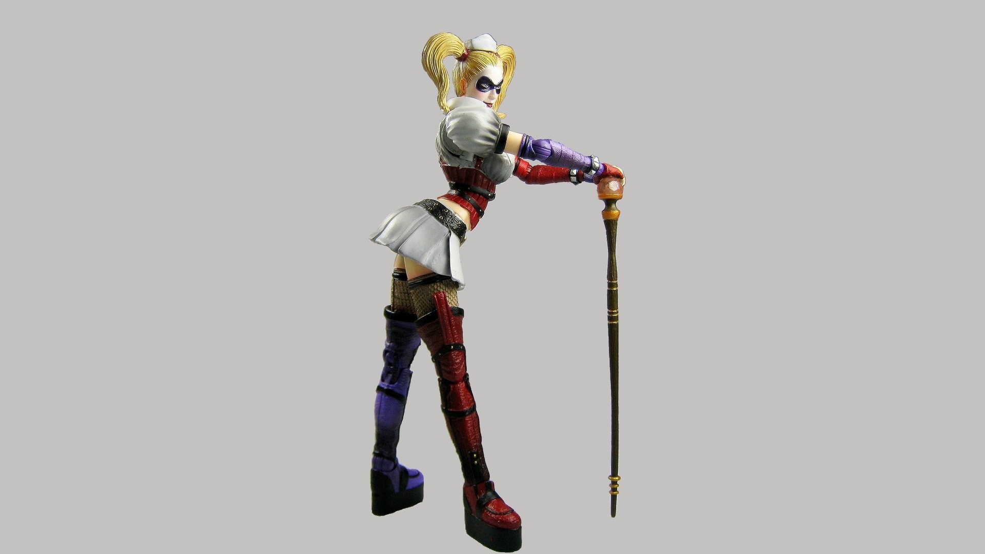 HD PC desktop wallpaper featuring Harley Quinn from the video game Batman: Arkham Asylum, posed with a cane against a plain gray background.