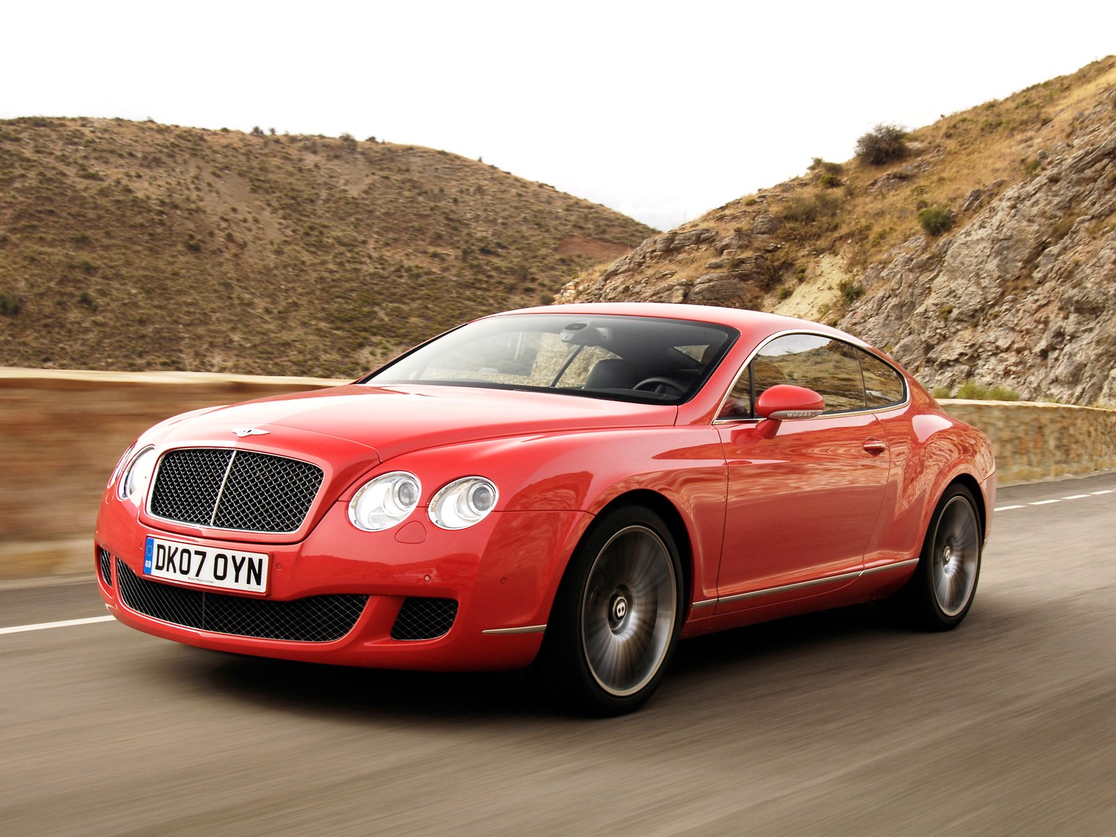 HD desktop wallpaper featuring a red Bentley Continental GT Speed cruising on a winding mountain road.