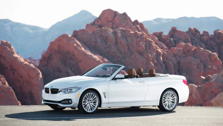White BMW 4 Series Cabrio convertible parked on a road with rocky red mountains in the background, featured as an HD PC desktop wallpaper and background.