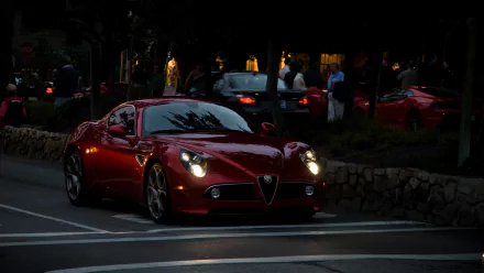 HD PC desktop wallpaper background: red Alfa Romeo 8C Competizione driving at dusk on a city street, headlights on and reflections gleaming across its glossy hood.