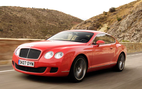 HD desktop wallpaper featuring a red Bentley Continental GT Speed cruising on a winding mountain road.