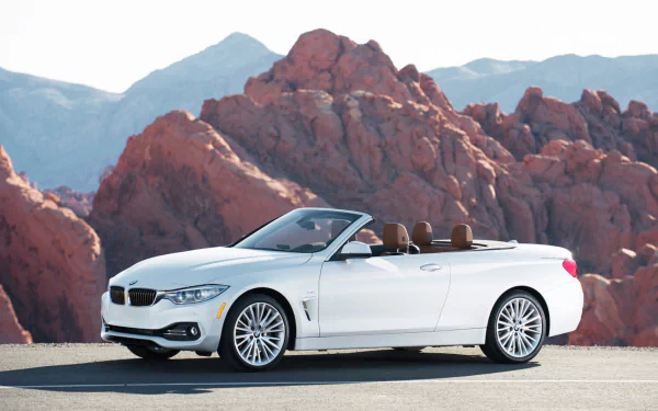 White BMW 4 Series Cabrio convertible parked on a road with rocky red mountains in the background, featured as an HD PC desktop wallpaper and background.