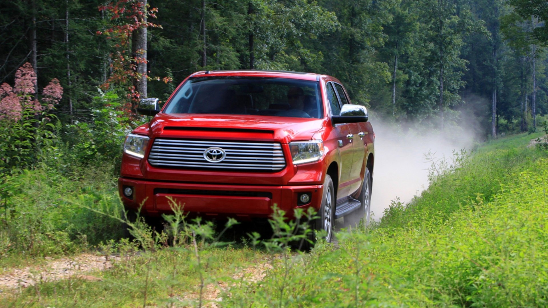 A red Toyota Tundra driving on a dirt road through a forest, captured in an HD PC desktop wallpaper and background.