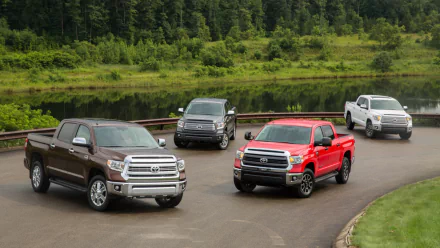 HD PC desktop wallpaper featuring four Toyota Tundra trucks in various colors parked on a curved road near a lush green forest and pond backdrop.