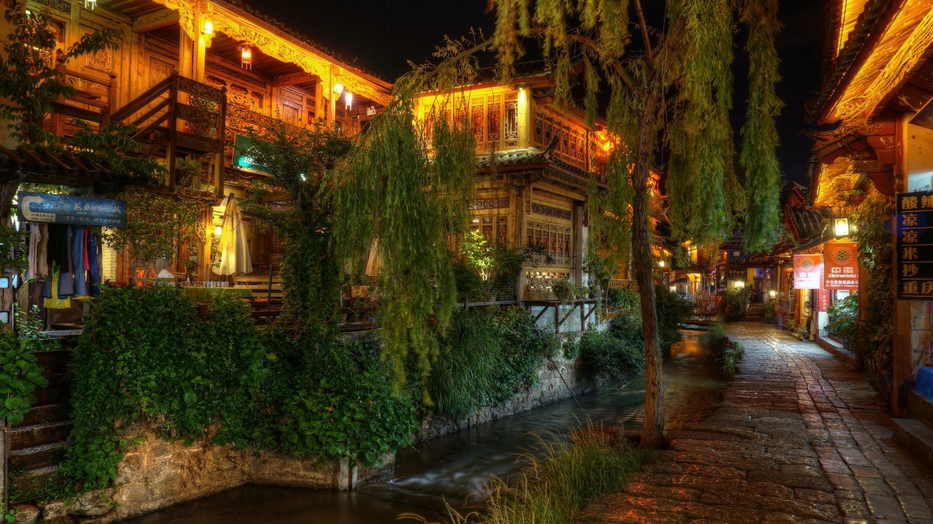 Night view of a man-made wooden building beside a narrow waterway in Lijiang, captured in stunning 4K Ultra HD.