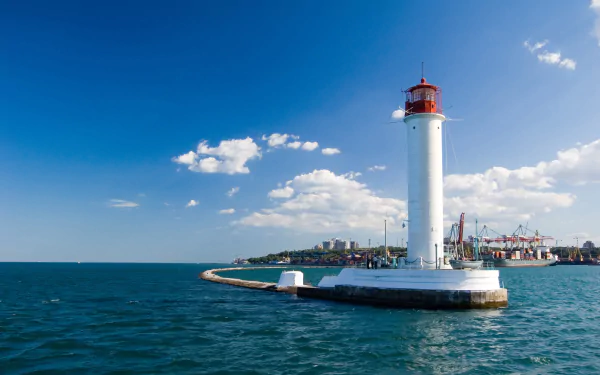 2K Quad HD desktop wallpaper of a man-made lighthouse on a curved breakwater jutting into the blue sea under a bright sky, with a coastal town on the horizon.