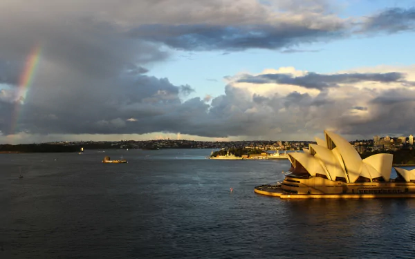 4K Ultra HD desktop wallpaper of Australia's man-made landmark, the Sydney Opera House, glowing on Sydney Harbour beneath dramatic clouds and a faint rainbow.