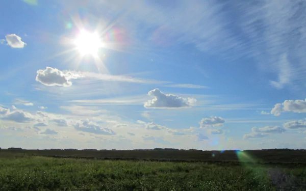 Bright sun shining over a green field under a blue sky with scattered clouds, captured in stunning 4K Ultra HD for a nature landscape desktop background.