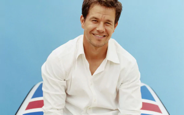 HD desktop wallpaper featuring American actor and celebrity Mark Wahlberg smiling against a light blue background with a patterned surface below.