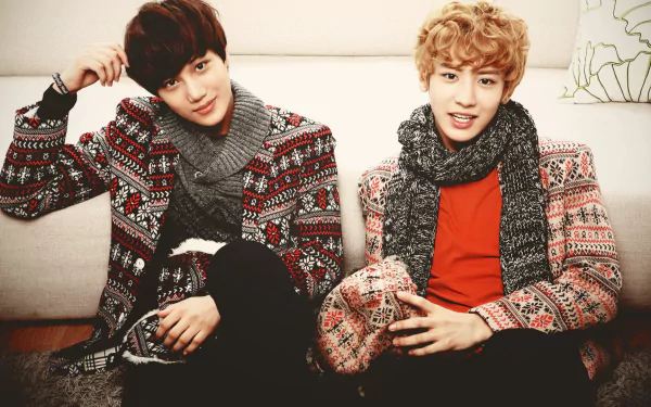 Two members of EXO, a music group, sit on a couch wearing patterned sweaters and scarves. This HD desktop wallpaper showcases a warm, cozy atmosphere.