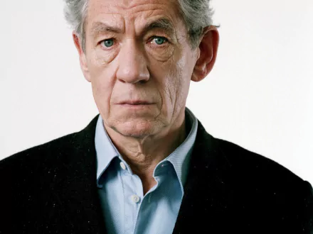 HD desktop wallpaper featuring a portrait of a distinguished elderly man with grey hair and piercing blue eyes, wearing a black jacket over a blue shirt.