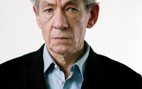 HD desktop wallpaper featuring a portrait of a distinguished elderly man with grey hair and piercing blue eyes, wearing a black jacket over a blue shirt.
