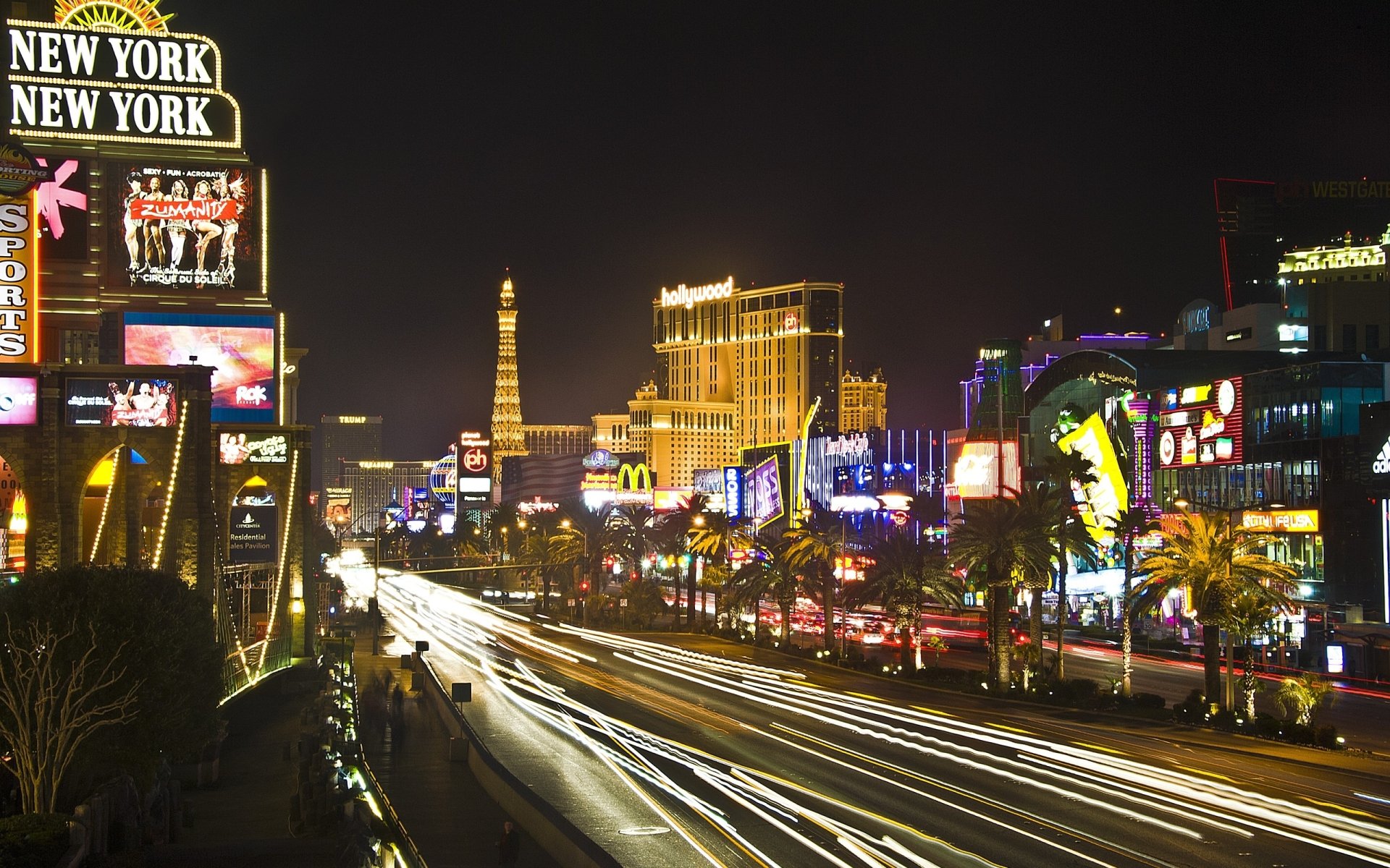 Nighttime view of Las Vegas Strip with bright neon signs, illuminated buildings, and streaks of car lights, captured as an HD man-made cityscape wallpaper background.
