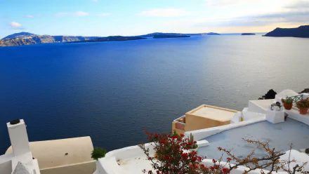 A stunning view of the blue sea and sky over Santorini, Greece, framed by white architecture and vibrant flowers, creating a breathtaking man-made landscape.