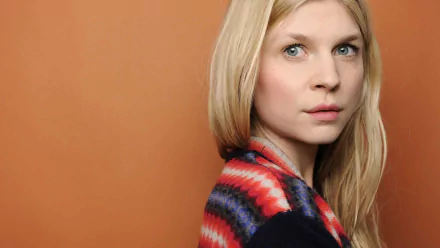 HD PC desktop wallpaper: portrait of a blonde woman in a colorful patterned shawl, looking over her shoulder against a warm orange background.