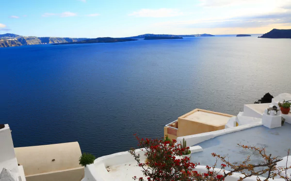 A stunning view of the blue sea and sky over Santorini, Greece, framed by white architecture and vibrant flowers, creating a breathtaking man-made landscape.