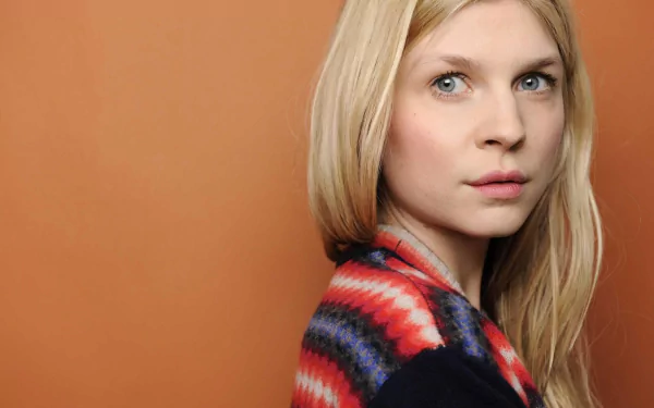 HD PC desktop wallpaper: portrait of a blonde woman in a colorful patterned shawl, looking over her shoulder against a warm orange background.