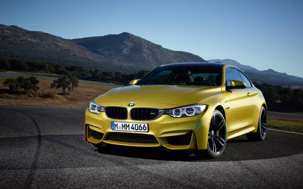 HD PC desktop wallpaper featuring a vibrant yellow BMW M4 Coupe parked on a scenic mountain road under a clear blue sky.