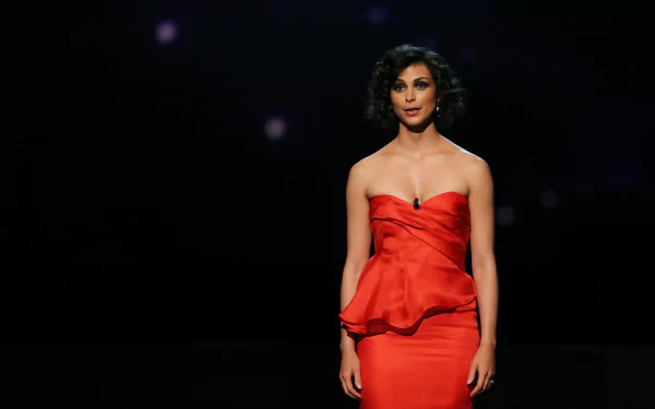 Brazilian actress and celebrity Morena Baccarin stands confidently in a strapless red dress against a dark background, captured in 4K Ultra HD quality.