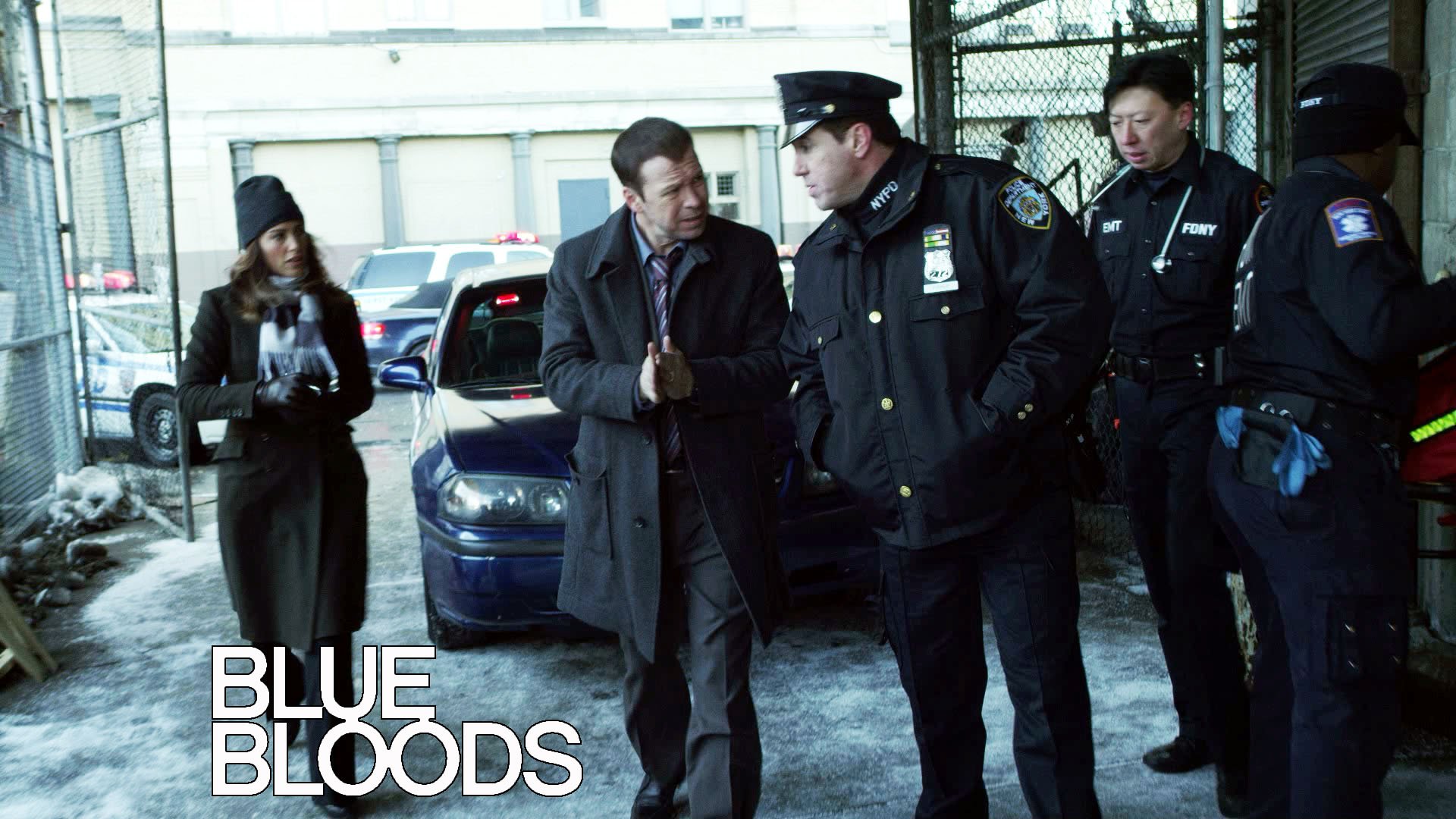 HD PC desktop wallpaper for the TV show Blue Bloods: uniformed NYPD officers converse by squad cars in a snowy gated lot, series logo in the lower-left.
