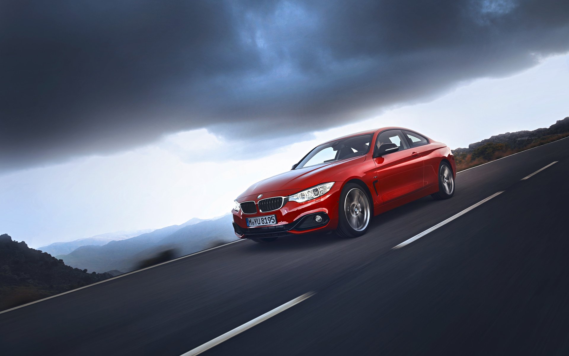 Red BMW 4 Series Coupe driving on a winding road under a dramatic stormy sky — 2K Quad HD PC desktop wallpaper/background.